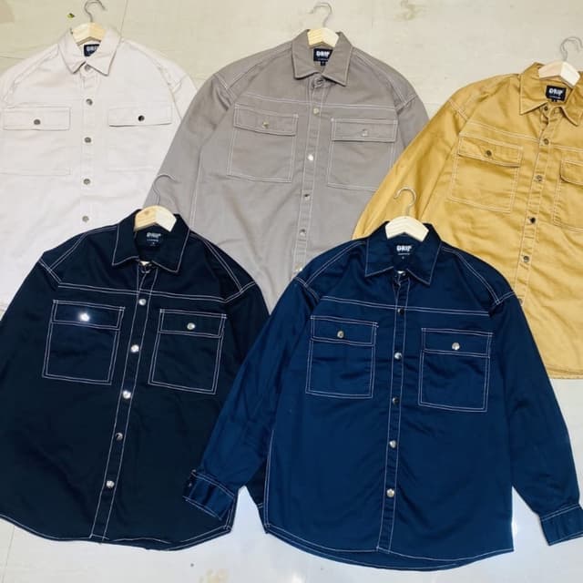 Variety of solid colors including: beige, grey, black, blue, and mustard yellow. All feature white stitching. Shirt