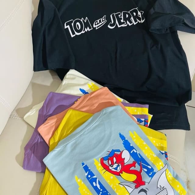 Variety of colors including black, white, purple, peach, yellow, and light blue. The shirts feature cartoon-themed prints with bright colors like red, yellow, blue, and white. T-shirts