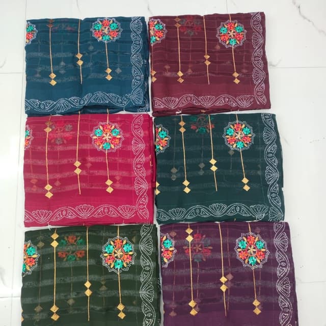 Various jewel tones including teal, burgundy, deep red, emerald green, and purple, with accents of gold and a contrasting white/cream border Saree