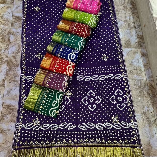 Purple with white and gold accents. Bundles of fabrics in pink, green, brown, red, dark green, blue, and purple. Saree or similar ethnic fabric