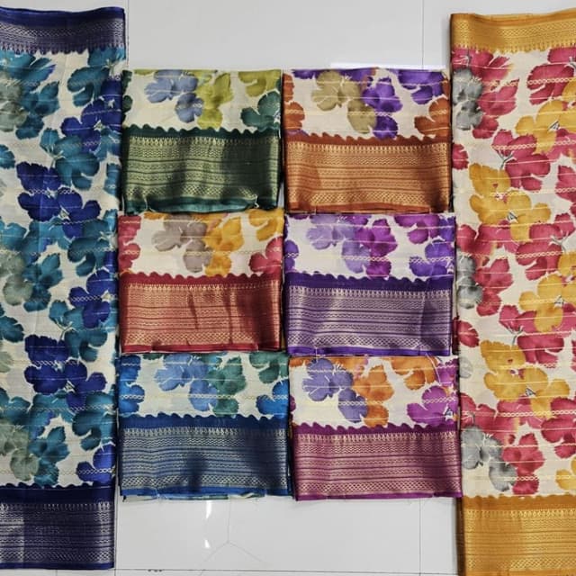 Various floral patterns on a white base, with accents of blue, green, yellow, orange, and purple. Borders feature gold, green, blue, and reddish-brown hues. Saree
