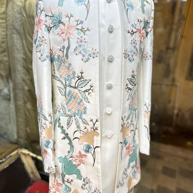 Ivory white with pastel floral embroidery in shades of pink, blue, teal, and peach, accented by green leaves and brown vines. Jacket/Sherwani