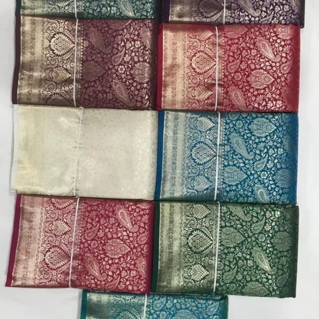 Various rich jewel tones including emerald green, burgundy, teal, purple, and cream, with metallic accents of gold or silver. Saree