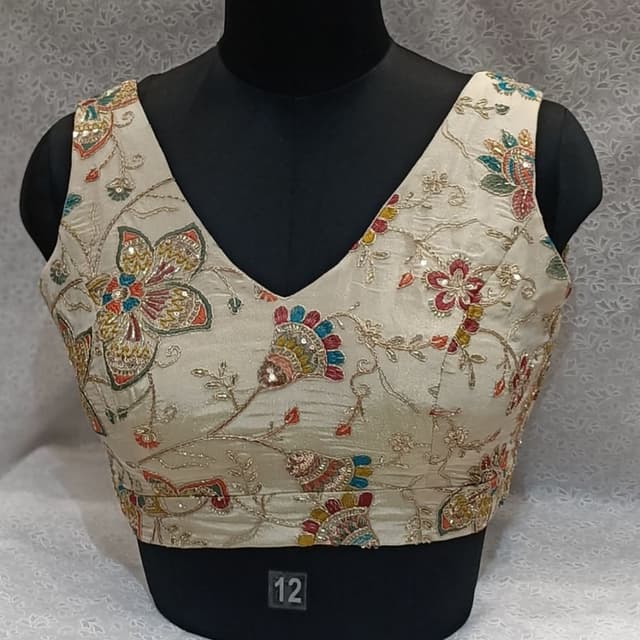 Cream base with multi-colored floral and vine embroidery in red, blue, green, yellow, and gold threads. Accented with shimmering sequins. Blouse
