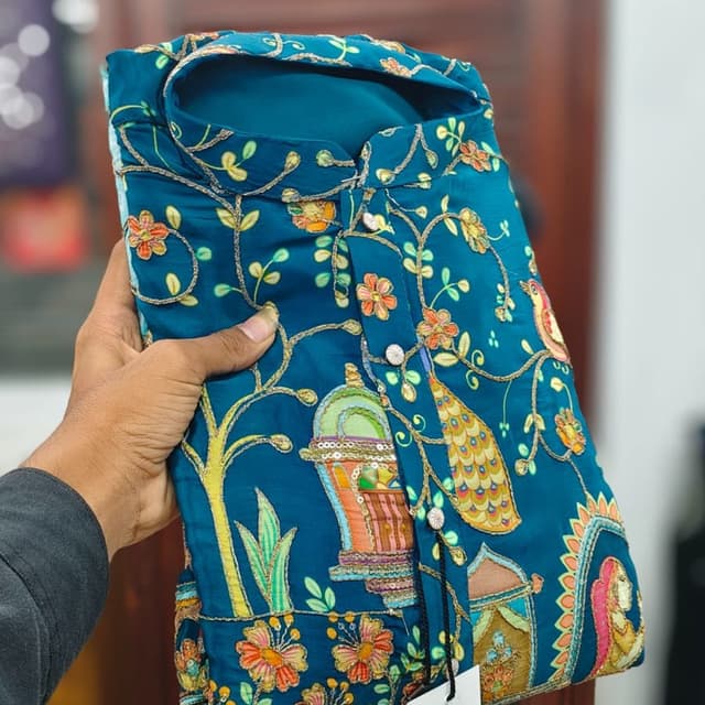Teal base with multicolored floral and architectural accents including orange, pink, yellow, and green Kurti