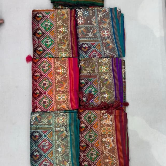 Multi-colored with earthy base tones like brown, accented with vibrant hues including red, green, orange, teal, and magenta. Saree